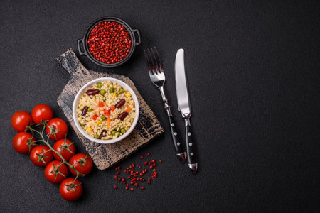 Boiled wheat bulgur porridge with vegetables peppers, peas, corn on a dark concrete backgroundの写真素材