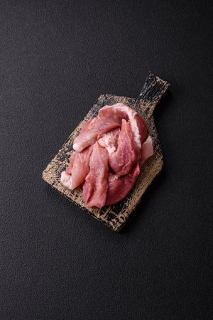 A piece of raw fresh pork on a wooden cutting board with spices and herbs on a dark concrete backgroundの写真素材