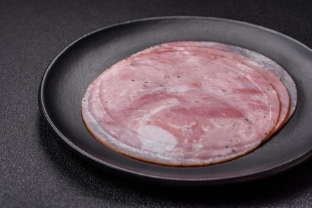 Ham cut into round slices with salt, spices and herbs on a dark textured background