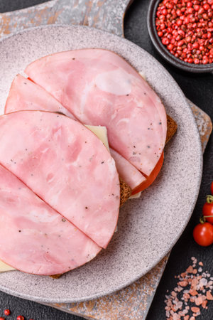 Sandwich with toast, ham, cheese, tomatoes, salt, spices and herbs on a dark textured backgroundの写真素材
