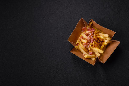 Crispy French fries with pieces of bacon, salt and spices on a dark concrete background