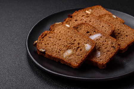 Brown bread with seeds, grains, salt and spices on a dark concrete background