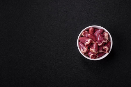 Raw chicken hearts with salt, spices and herbs on a dark backgroundの写真素材