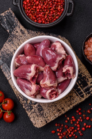 Raw chicken hearts with salt, spices and herbs on a dark concrete background
