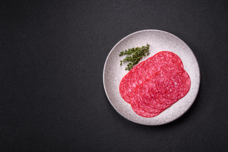 Smoked salami sausage with salt, spices and herbs cut into slices on a dark concrete backgroundの写真素材