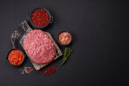 Fresh raw ground beef burger patty with salt and spices on textured concrete background
