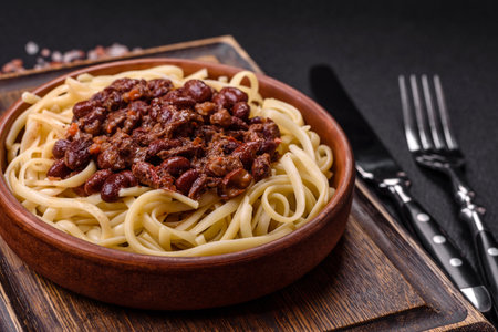 Rice noodles with beans, meat, tomato sauce, spices and herbs on a dark concrete backgroundの写真素材