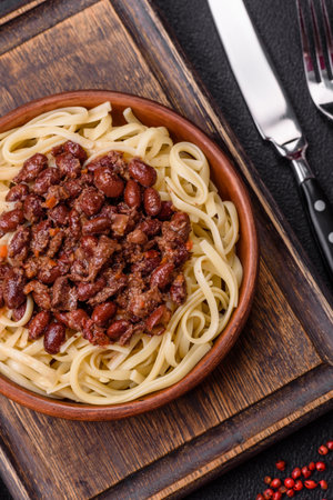 Rice noodles with beans, meat, tomato sauce, spices and herbs on a dark concrete backgroundの写真素材