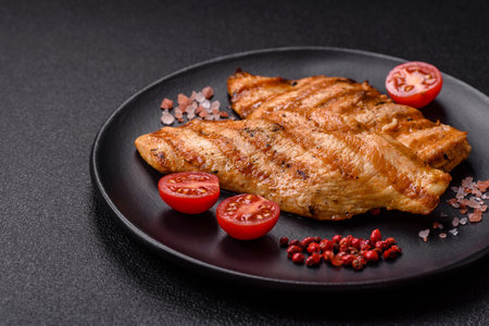 Juicy chicken fillet baked on the grill with salt, spices and herbs on a dark concrete backgroundの写真素材