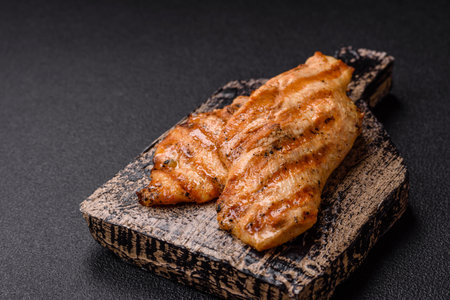 Juicy chicken fillet baked on the grill with salt, spices and herbs on a dark concrete backgroundの写真素材