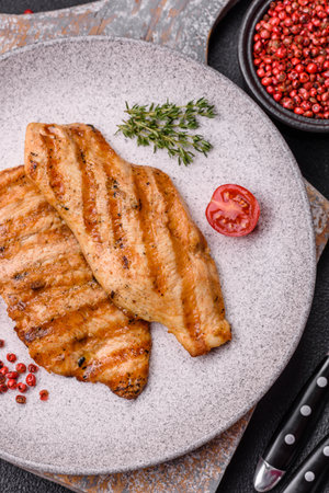 Juicy chicken fillet baked on the grill with salt, spices and herbs on a dark concrete backgroundの写真素材