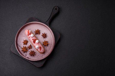 Sweet eclair or profiterole with strawberry custard on a dark textured background