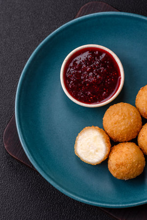 French fries balls with breaded brie or camembert cheese with sweet berry sauce on a dark concrete...