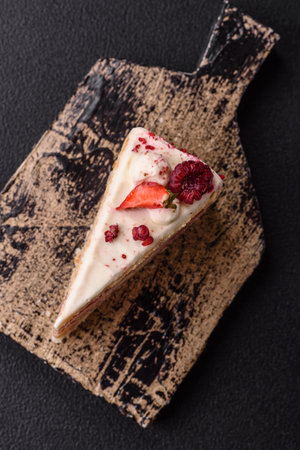 Piece of sweet layer cake with white cream, raspberries and strawberries on a dark concrete backgroundの写真素材