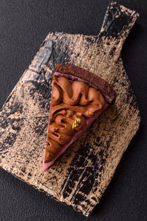 A piece of sweet cheesecake with strawberry flavor, covered with chocolate on a dark concrete backgroundの写真素材