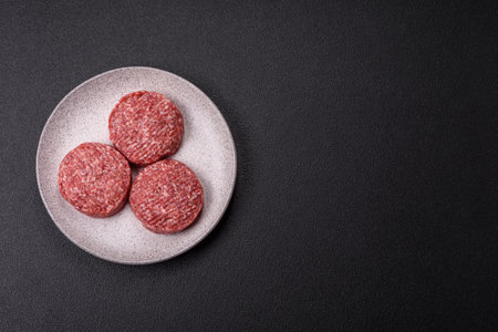 Fresh raw ground beef burger patty with salt and spices on textured concrete background