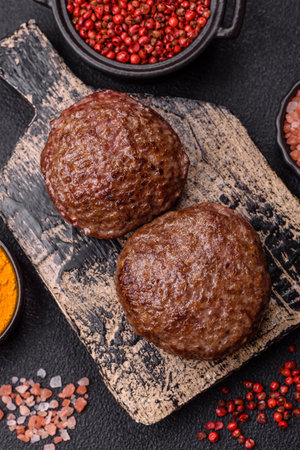 Beef burger patties with salt, spices and herbs grilled on a dark concrete background