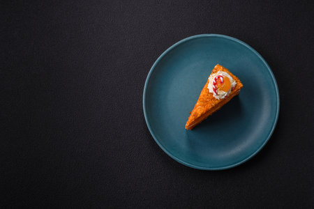 Piece of sweet layer cake with pumpkin or citrus flavor with cream on a dark textured backgroundの写真素材