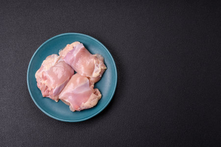 Fresh raw chicken thigh fillets with salt, spices and herbs on a dark concrete backgroundの写真素材