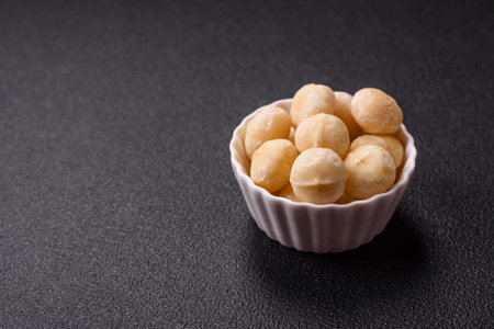 Delicious nutritious macadamia nuts in ceramic bowl on dark concrete backgroundの写真素材