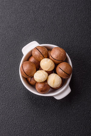 Delicious nutritious macadamia nuts in ceramic bowl on dark concrete backgroundの写真素材