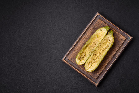 Delicious zucchini cut into two halves baked with salt, spices and herbs on a dark concrete backgroundの写真素材