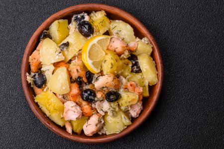 Baked salmon pieces with potatoes, olives with salt, spices and herbs on a dark concrete backgroundの写真素材