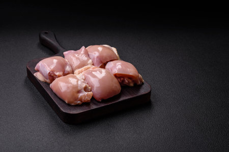 Fresh raw chicken thigh fillets with salt, spices and herbs on a dark concrete backgroundの写真素材