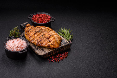 Delicious fresh grilled chicken fillet with spices and herbs on a dark concrete background. A dish cooked over fireの写真素材