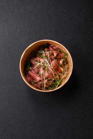Warm salad consisting of slices of roast beef, greens, tomatoes, cucumbers, green beans on a dark...