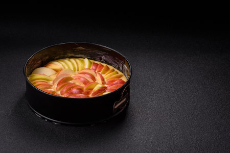 Raw sweet apple pie in a mold prepared for baking on a dark concrete background
