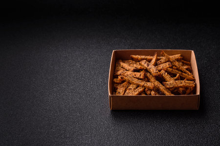 Crispy brown bread crackers or croutons with seeds and grains, salt, spices and herbs on a dark concrete backgroundの写真素材