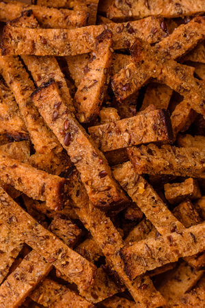 Crispy homemade brown bread crackers or croutons with seeds and grains, salt, spices and herbs on a dark concrete backgroundの写真素材