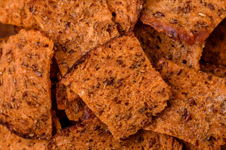 Crispy homemade brown bread chips with seeds and grains, salt, spices and herbs on a dark concrete...