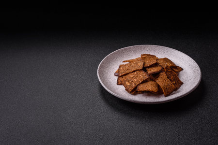 Crispy homemade brown bread chips with seeds and grains, salt, spices and herbs on a dark concrete backgroundの写真素材