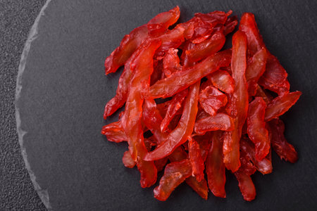 Dried chicken slices, jerky, with cherry or plum flavor, salt and spices on a dark concrete...
