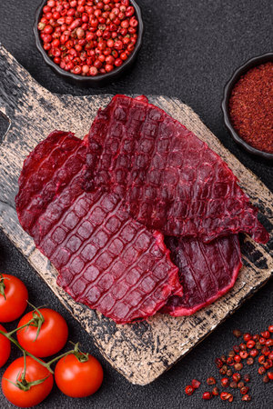 Dried beef slices, jerky, with salt and spices on a dark concrete backgroundの写真素材