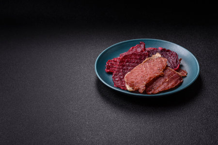 Jerky, dried pork meat slices with salt and spices on a dark concrete background