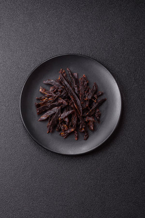 Jerky, dried beef slices with salt and spices on a dark concrete backgroundの写真素材