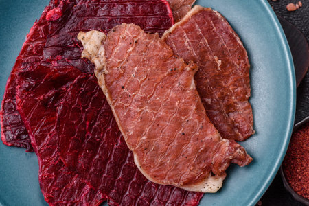 Dried pork meat slices with salt and spices on a dark concrete background