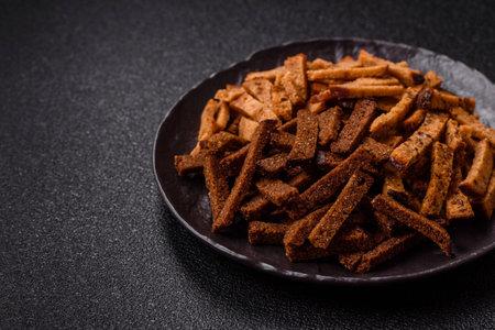 Crispy homemade brown bread crackers or croutons with seeds and grains, salt, spices and herbs on a dark concrete backgroundの写真素材
