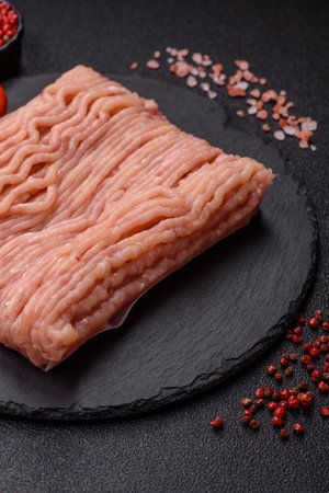 Raw minced chicken with salt, spices and herbs on a dark concrete background