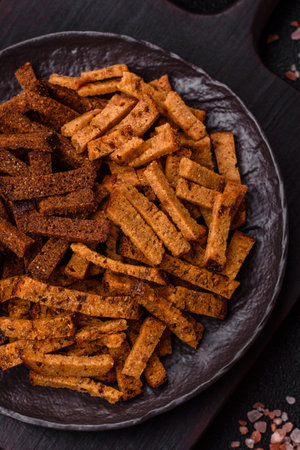 Crispy homemade brown bread crackers or croutons with seeds and grains, salt, spices and herbs on a dark concrete backgroundの写真素材