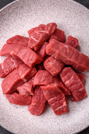 Raw beef tenderloin cut into slices with salt and spices on a dark concrete background