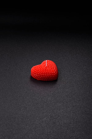 Red wax candle in the shape of a heart as decor for Valentine's Day on a dark concrete backgroundの写真素材