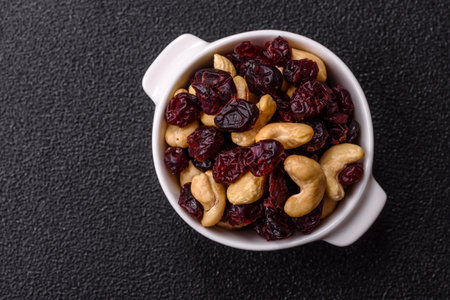 Mixture of roasted cashews and dried cranberries on a dark concrete background