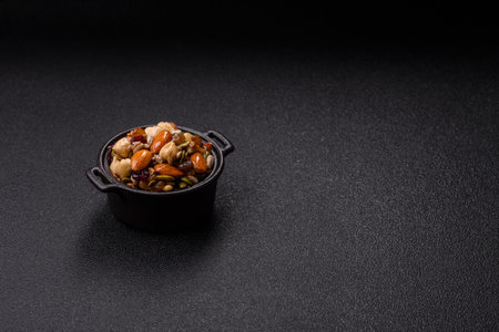 Cashew nuts, walnuts, hazelnuts, pine nuts and dried fruits in ceramic bowl on dark backgroundの写真素材