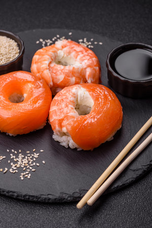 Donut shaped sushi rolls with salmon, shrimp and tuna, salt, spices and soy sauce on dark concrete backgroundの写真素材