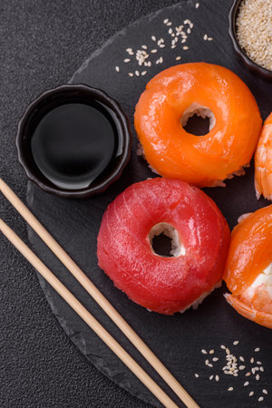 Donut shaped sushi rolls with salmon, shrimp and tuna, salt, spices and soy sauce on dark concrete backgroundの写真素材