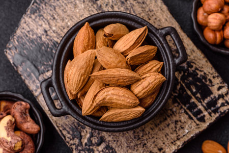 Roasted or raw almond nuts in shell in bowl on dark concrete backgroundの写真素材